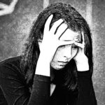 Een peinzende vrouw die haar handen in haar haar houdt, wat stress en de noodzaak voor rust symboliseert, in het artikel over de psyche van de moderne mens.